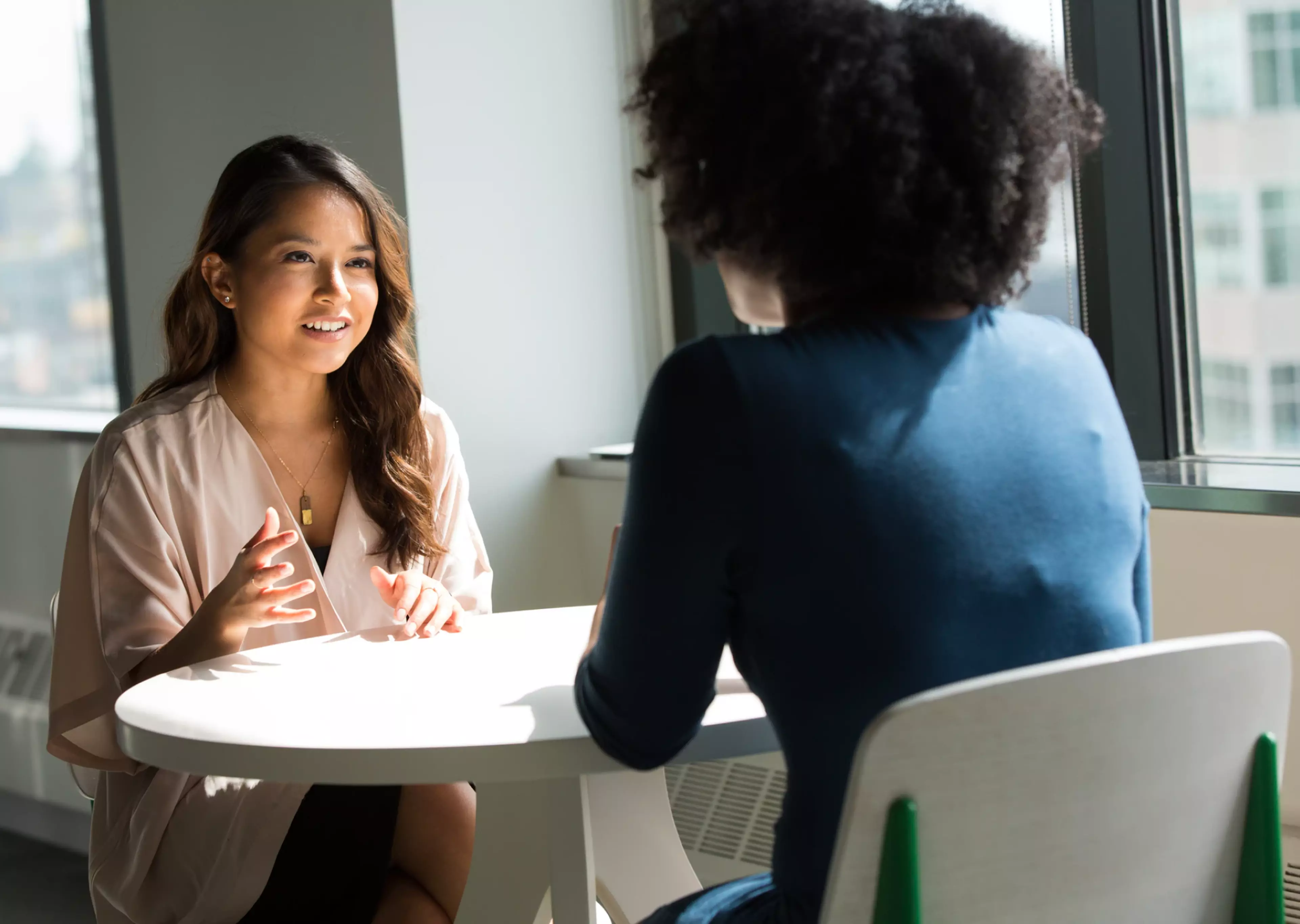 Two women seating at a table facing each other and talking.