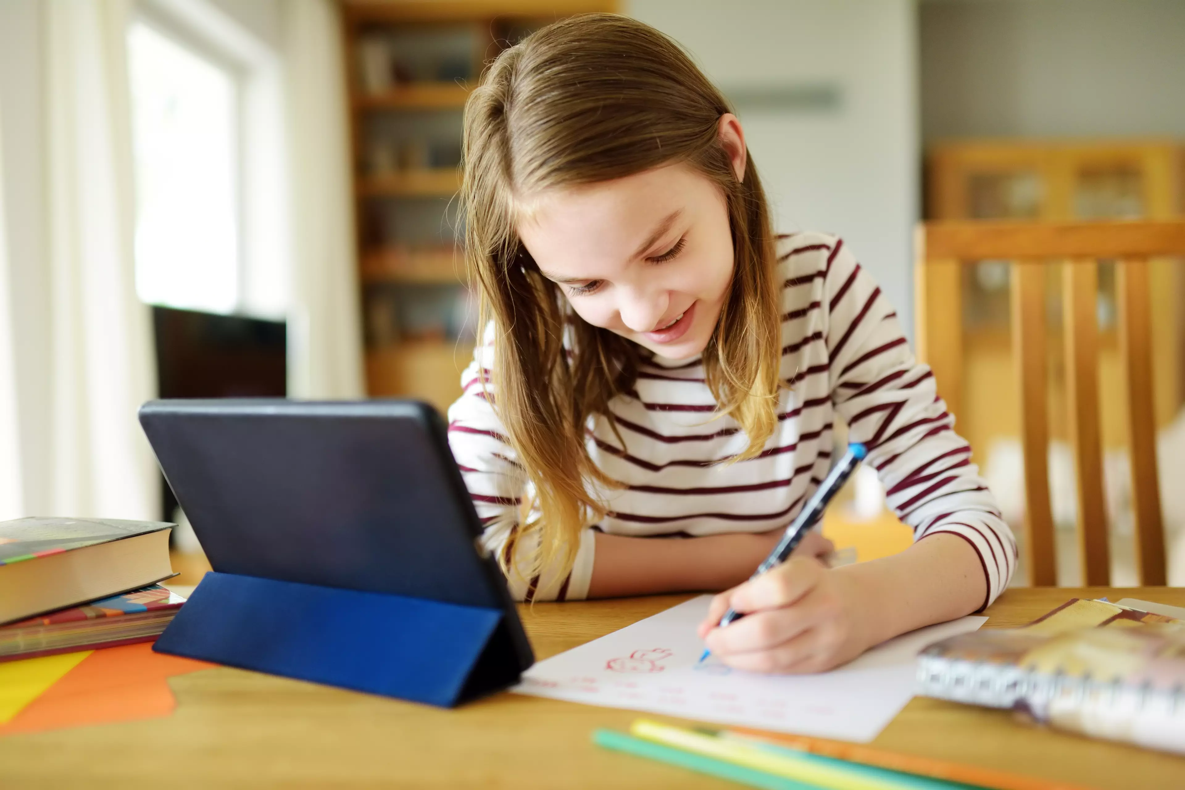 Young schoolgirls in front of a tablet, taking notes during online classes.