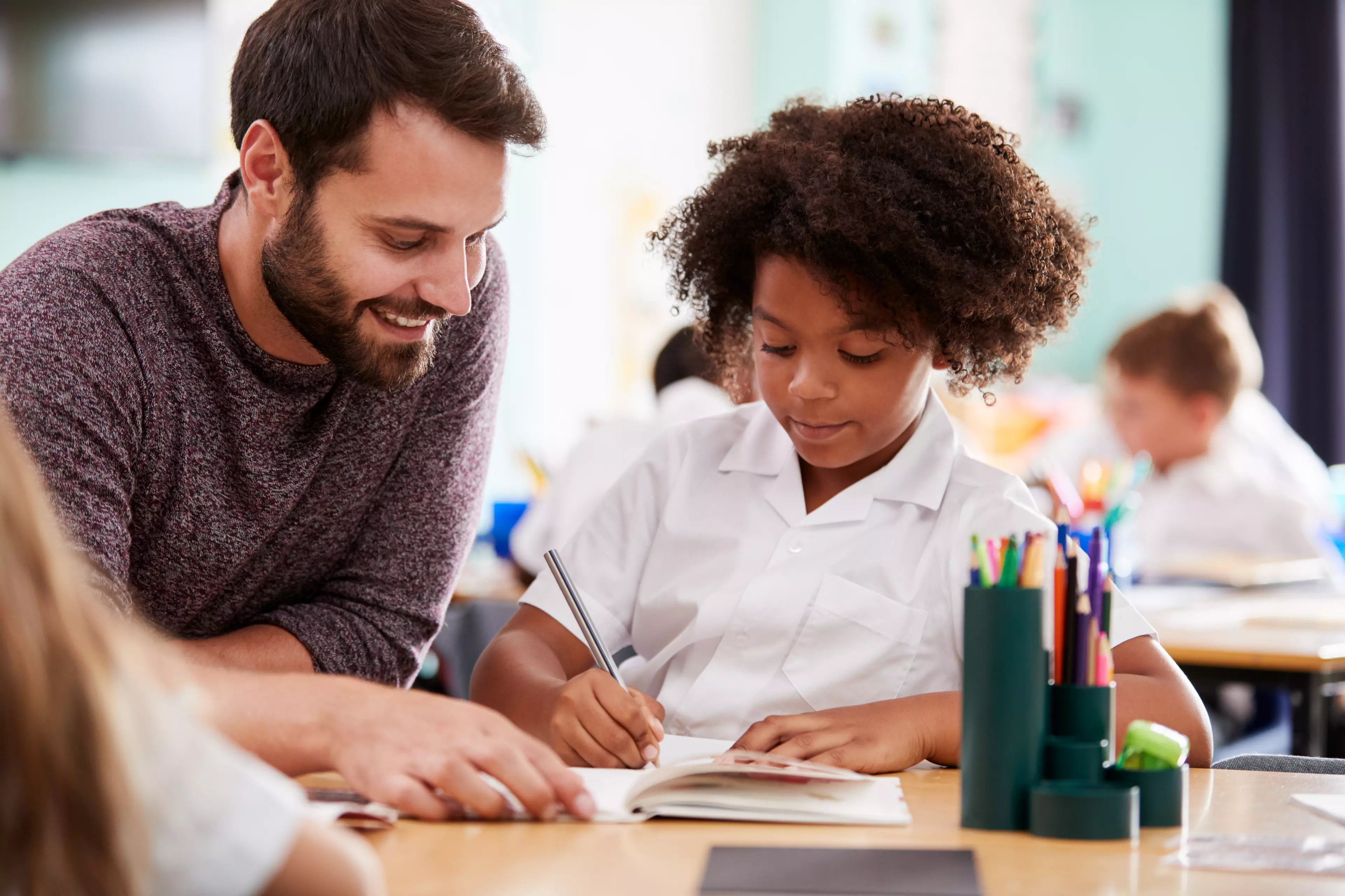 Smiling male teacher with a kid student sitting behind a desk