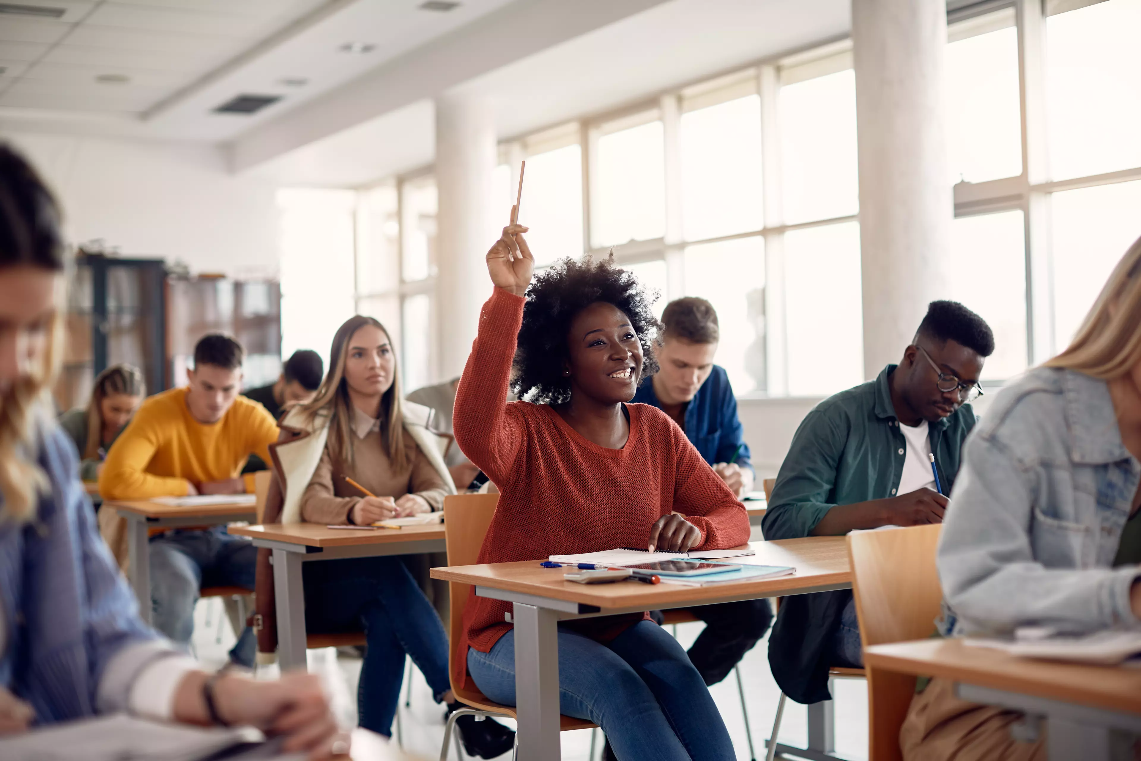 African-american woman in a classroom, raising hand to ask a question.