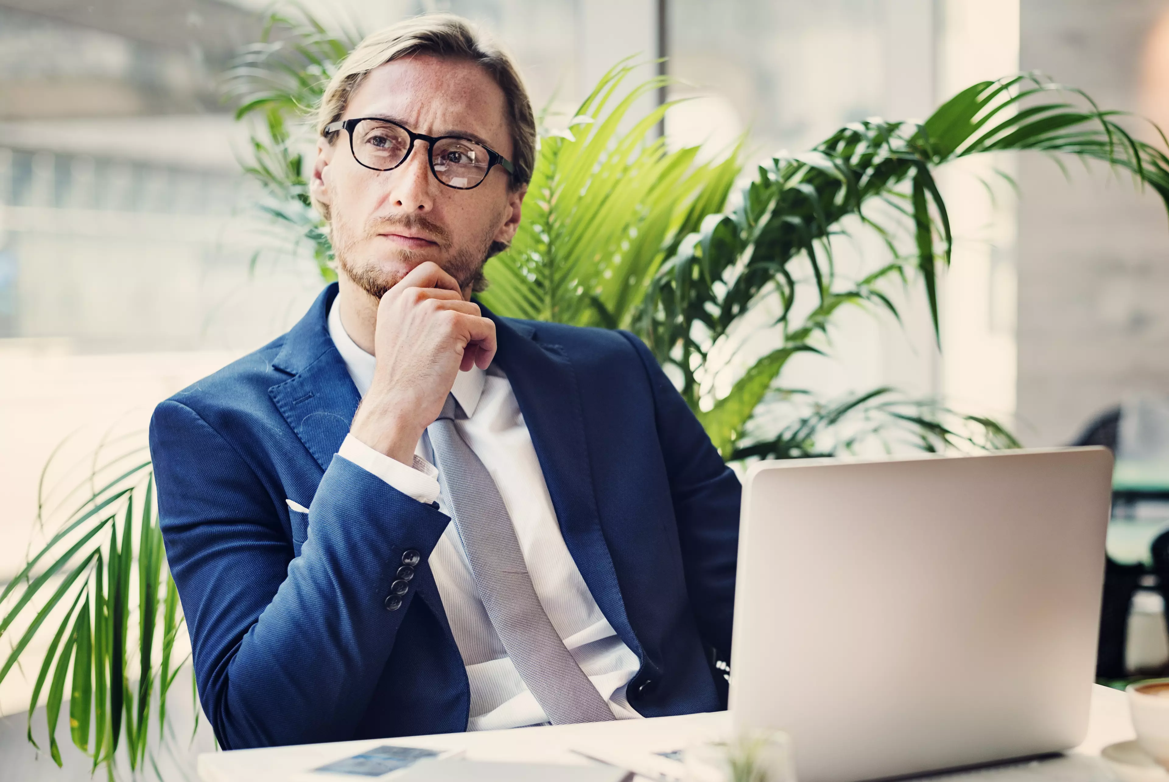 A mid-aged man wearing a suit, sitting in front of an open laptop.