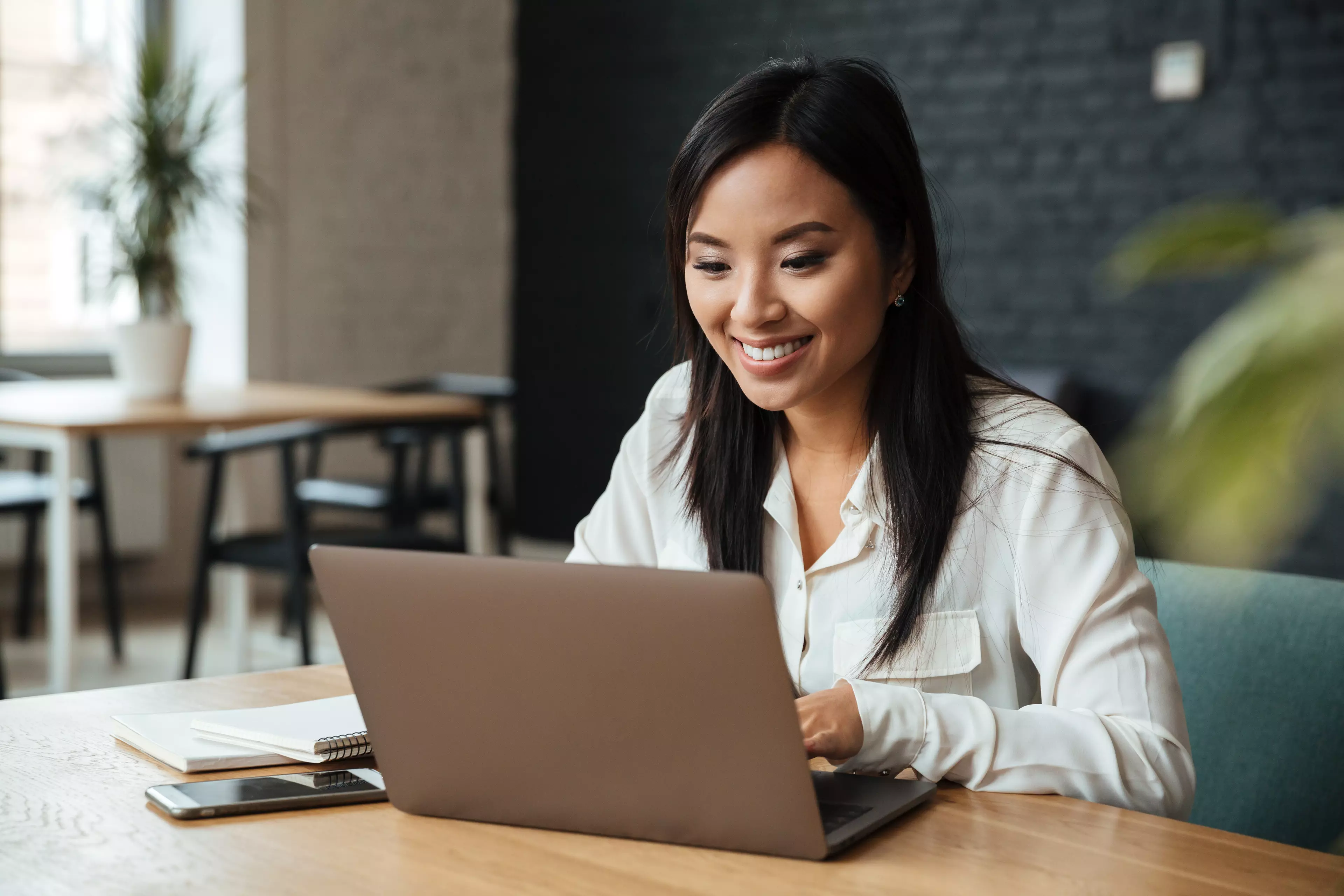 Smiling, dark-haired woman, sitting at a desk, typing on her notebook.