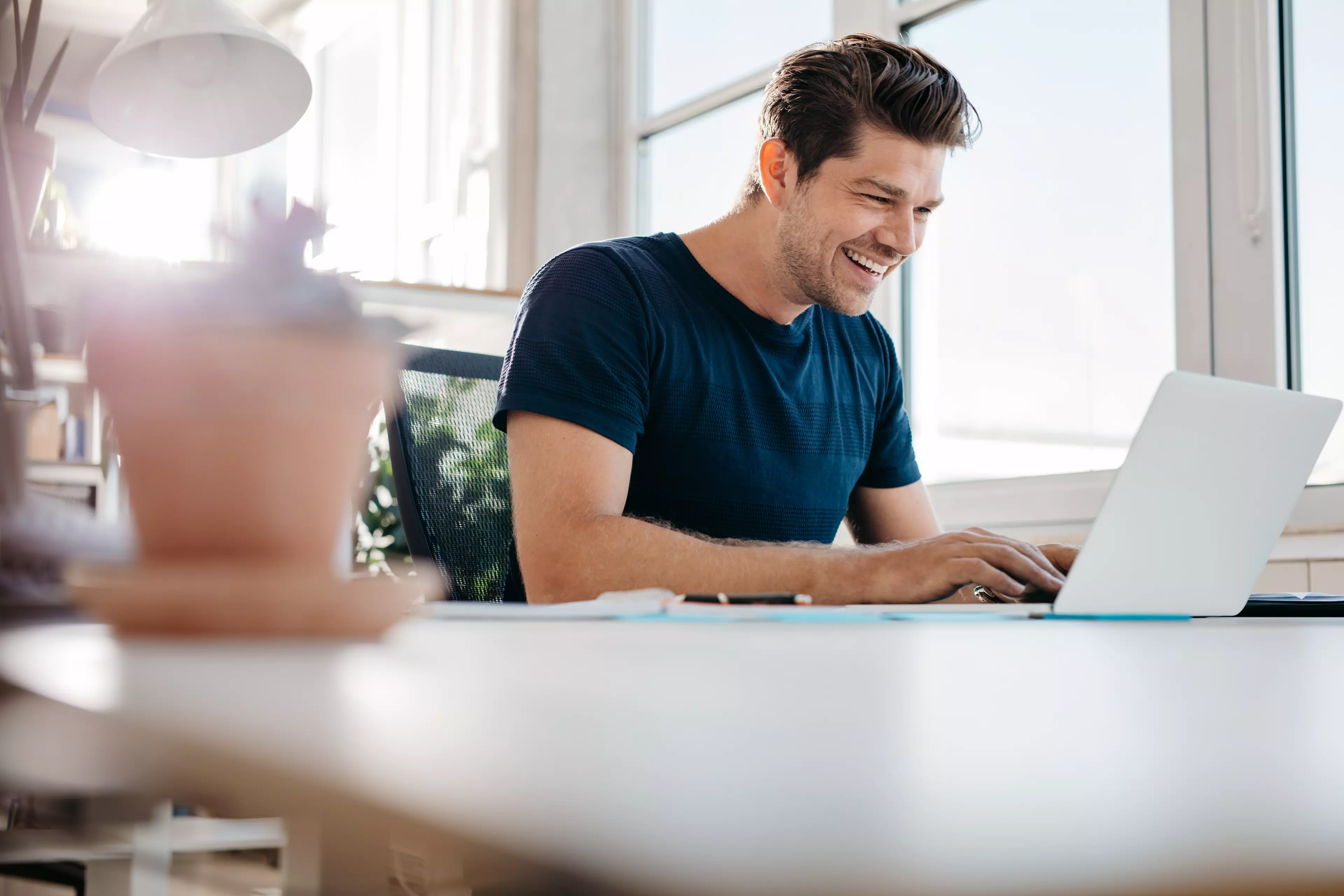 A smiling man sitting in front of a laptop