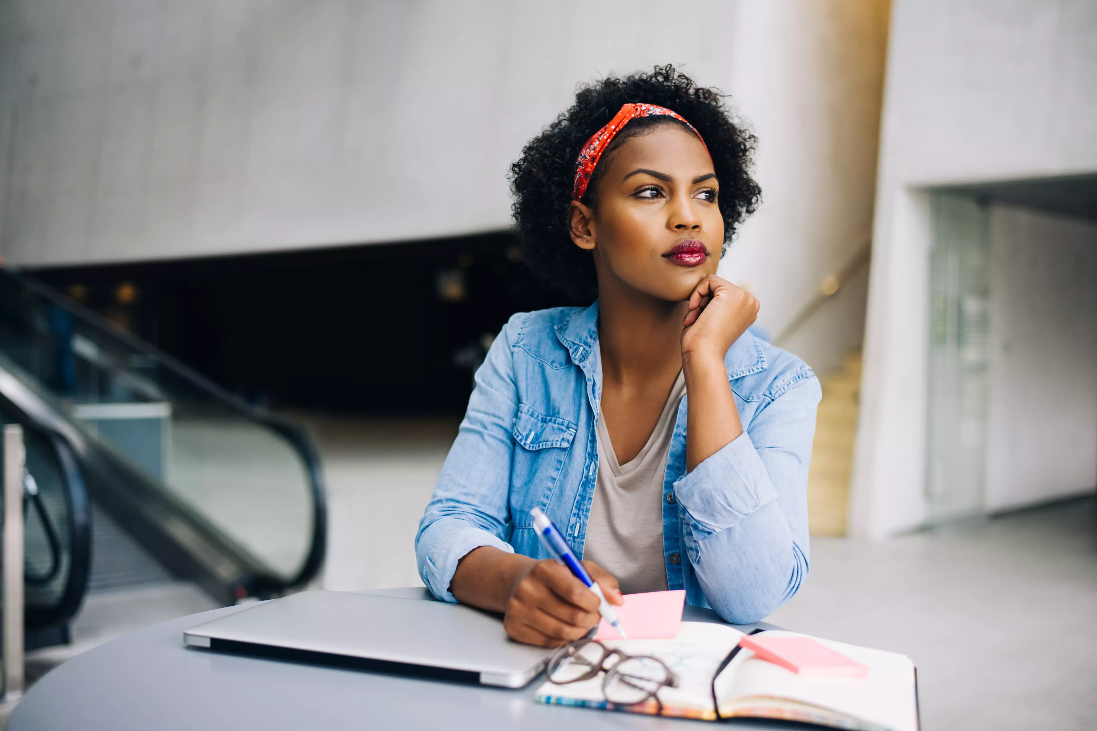 Dark-skinned woman sitting behind a desk with her laptop and notebook in front of her.