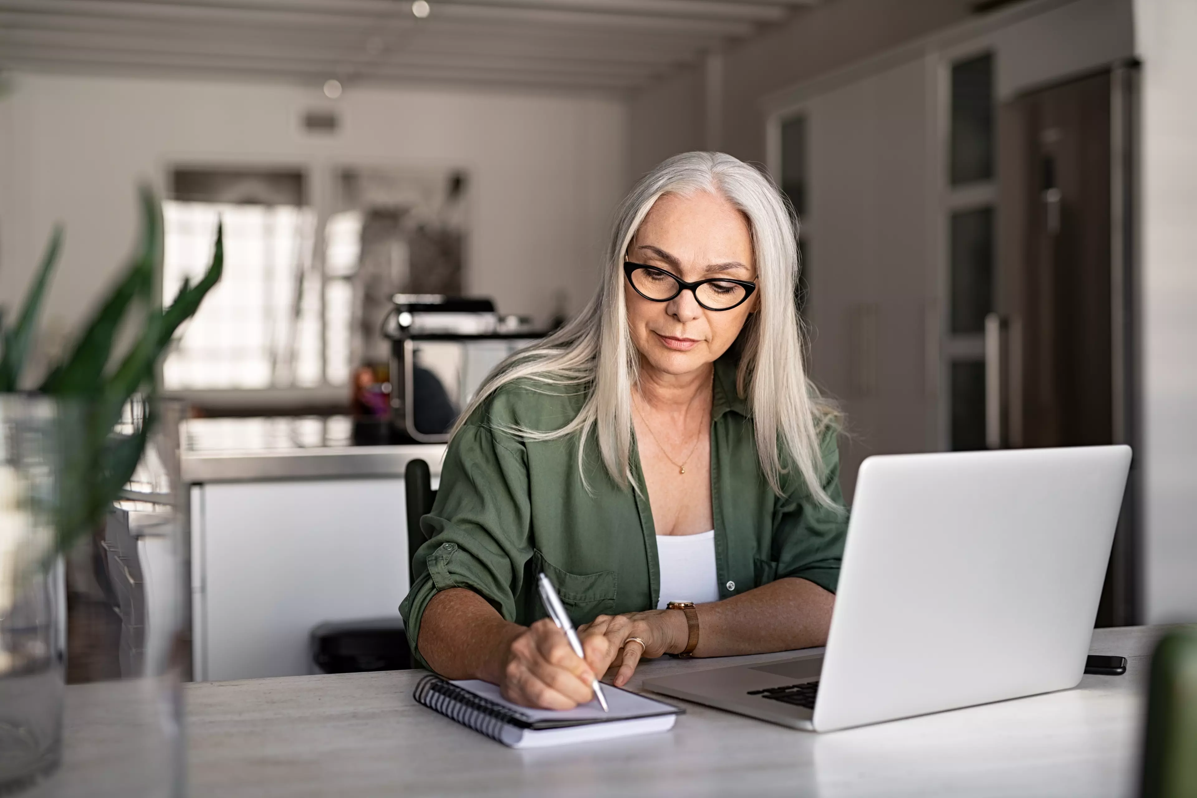 Long-hair woman in front of a laptop, writing in a notepad