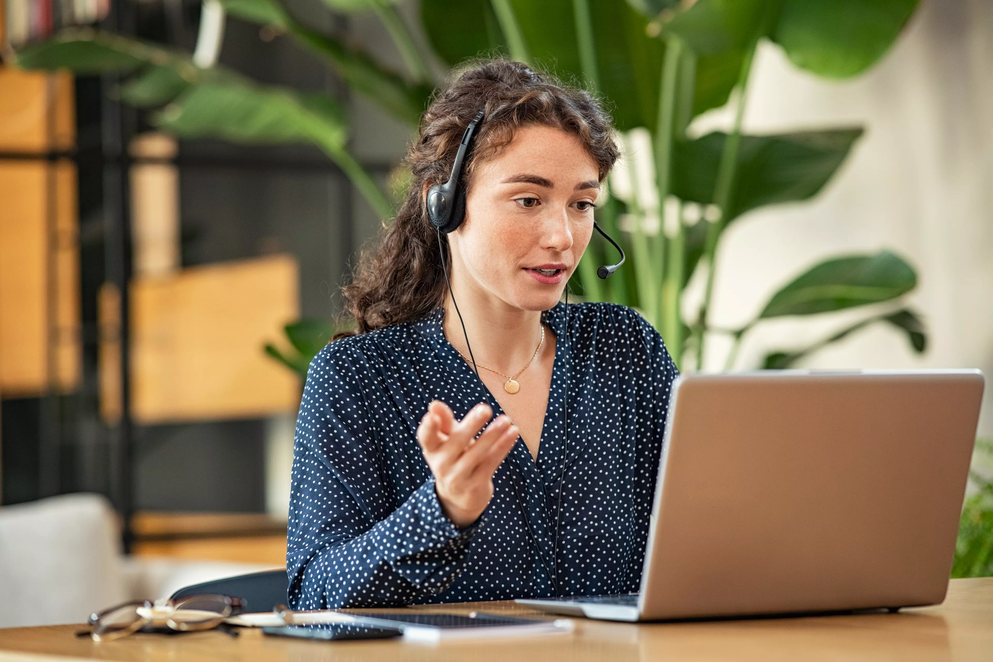  Young woman with a headset, talking over a teleconferencing app on her laptop.