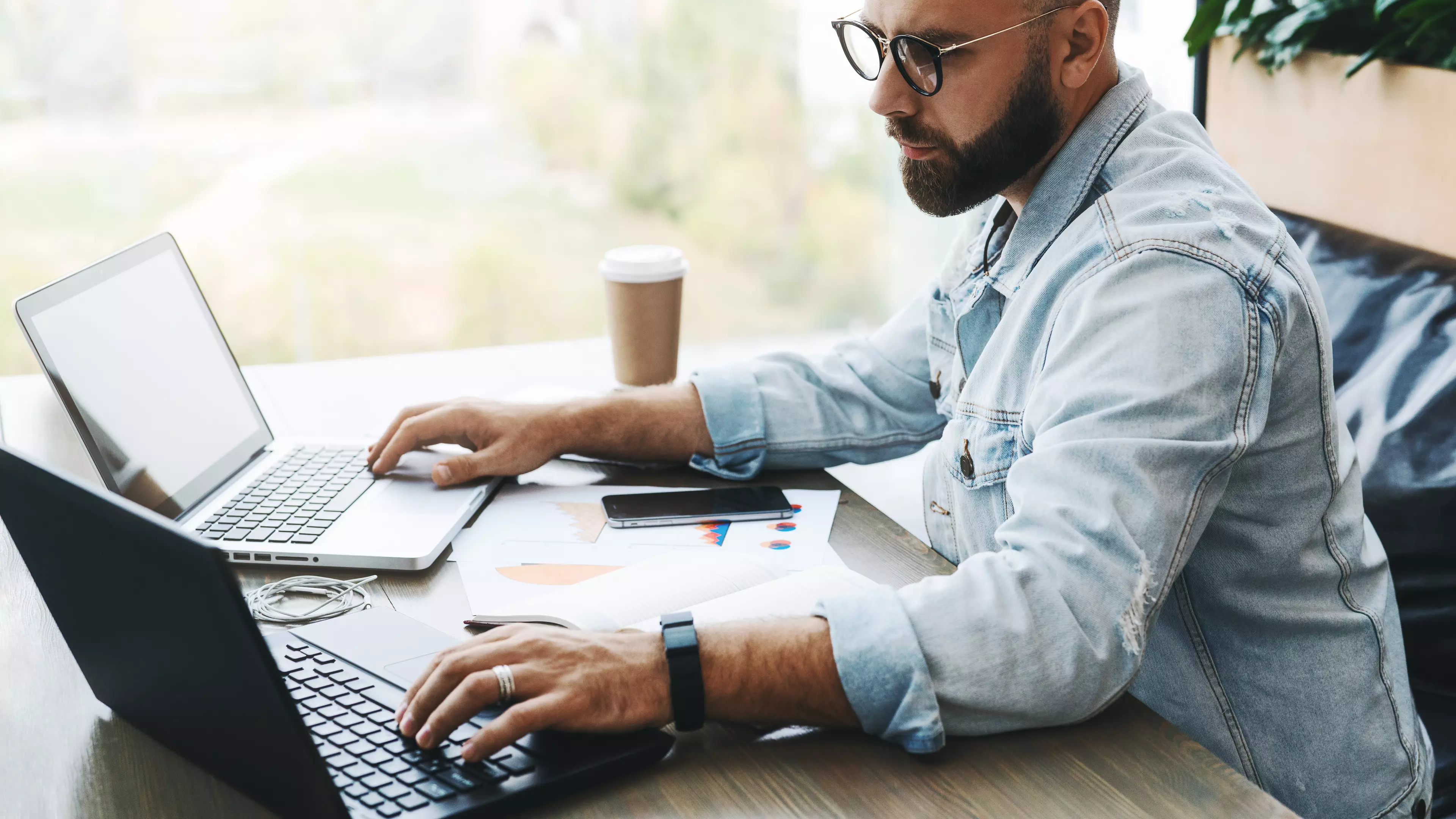 Young, bearded man sitting in front of two computers, cheating on online test