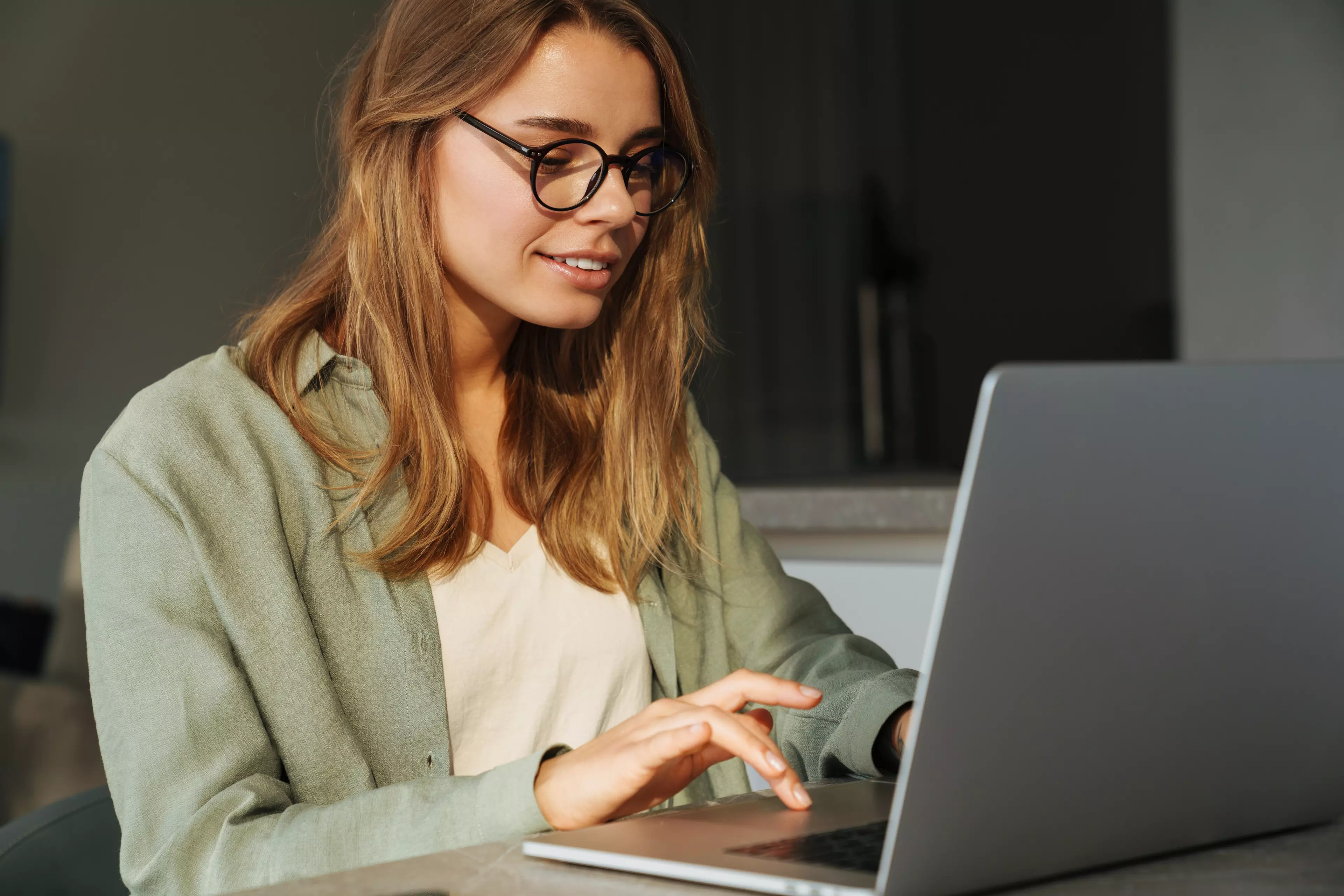  Young, long-haired woman sitting at a desk, typing on a laptop.