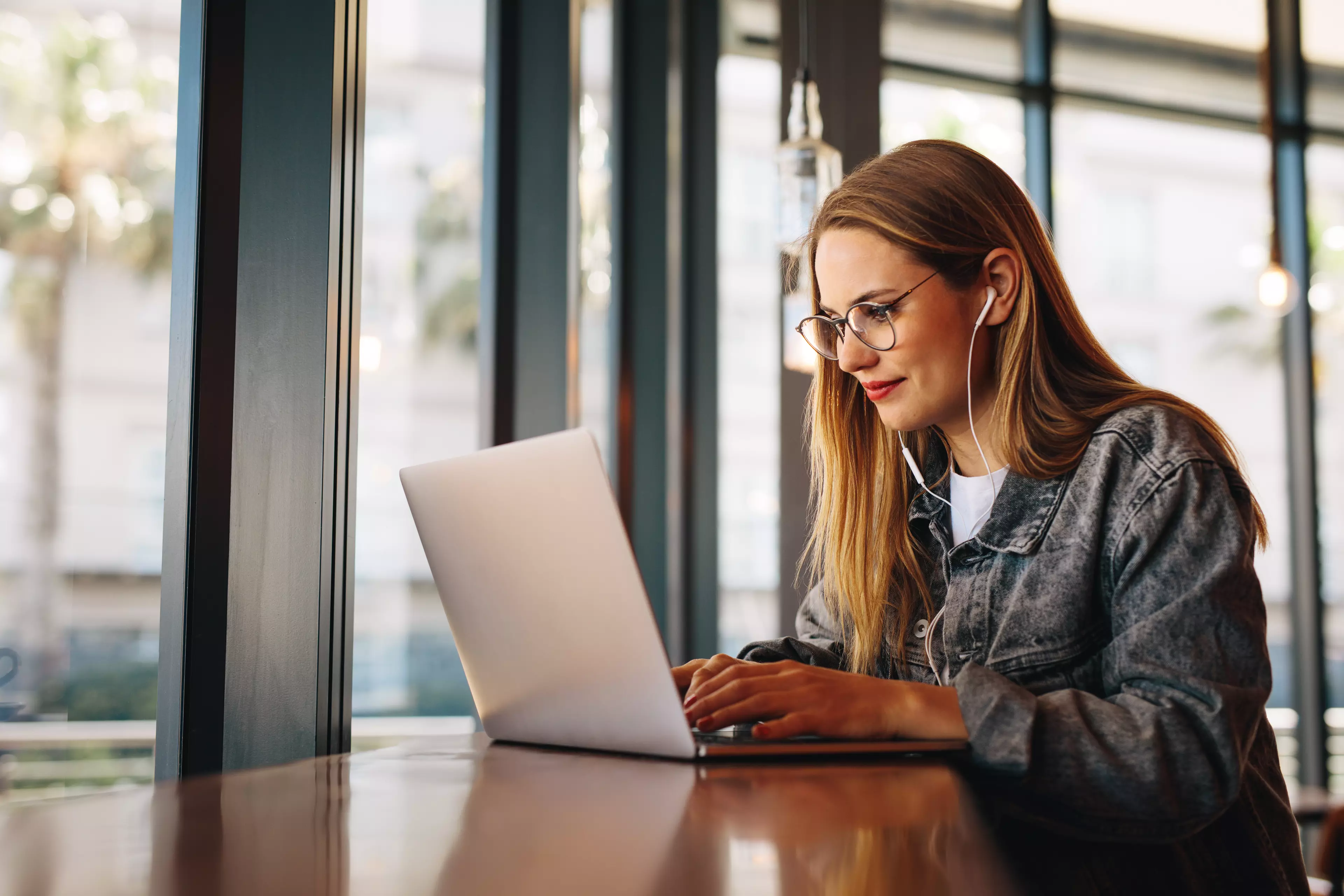  Young woman typing on her laptop with her headphones on.