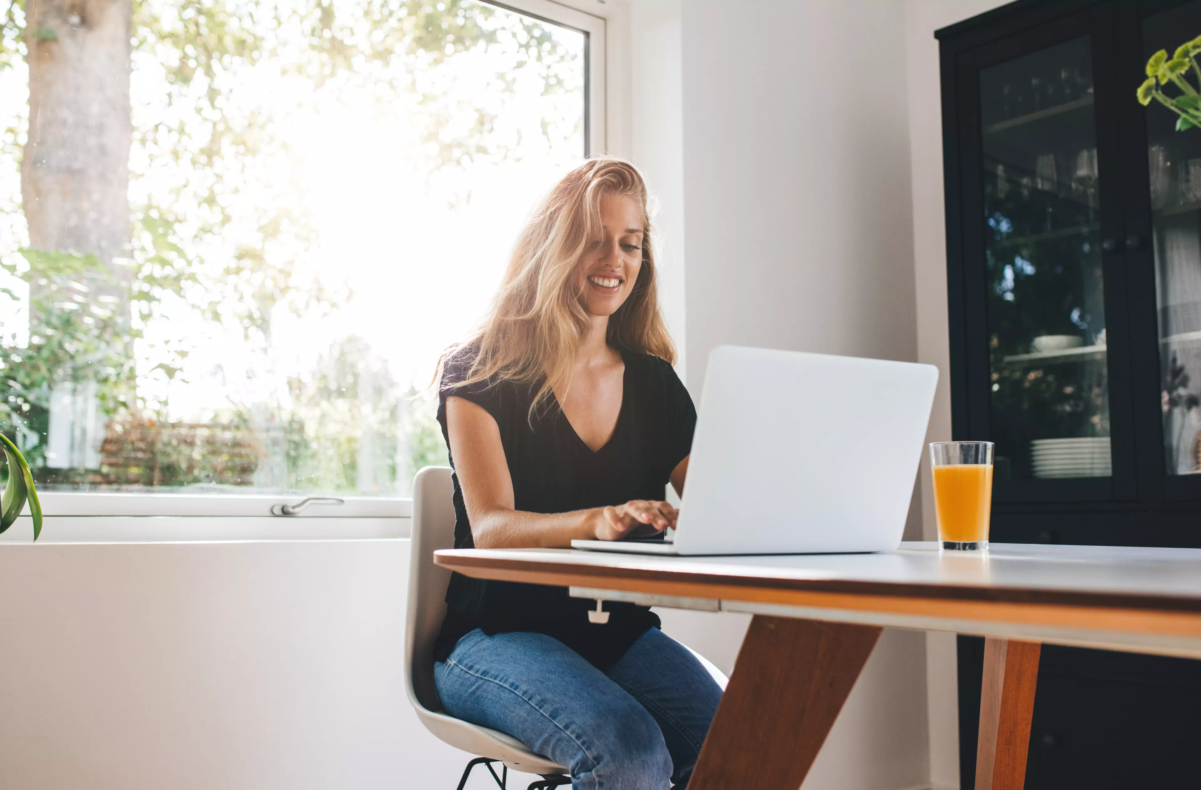  Young, smiling, blonde woman sitting at a table, working on a laptop.