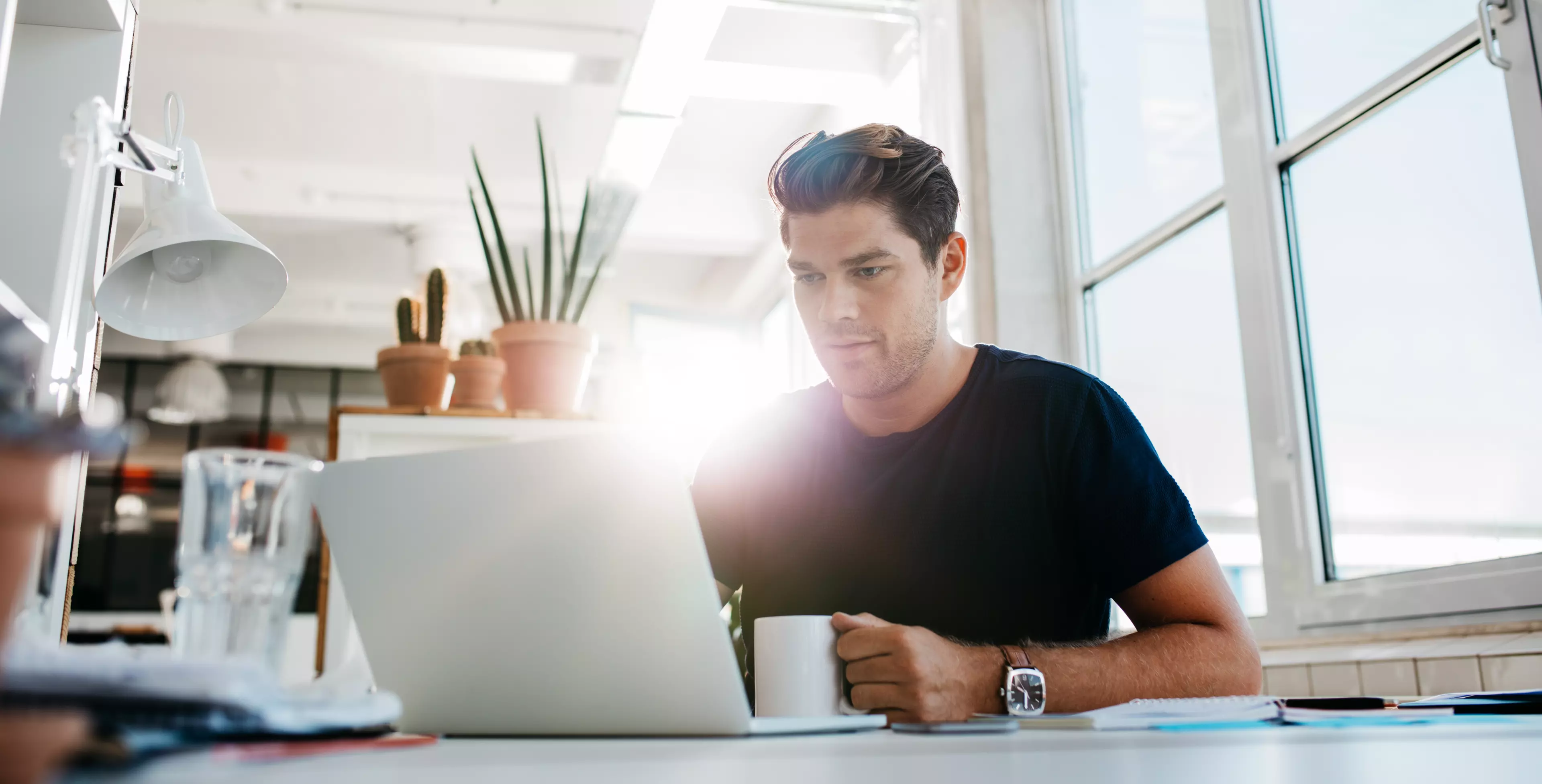  Young man sitting in front of a laptop, with a coffee in his hand.