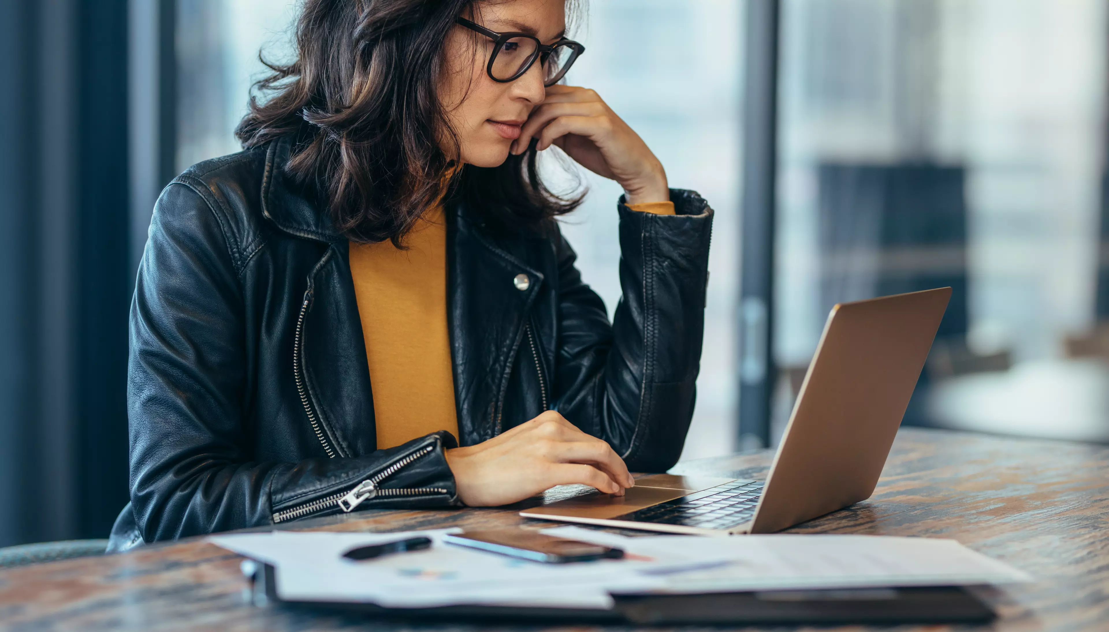 Woman in a leather jacket working on her laptop in an office.