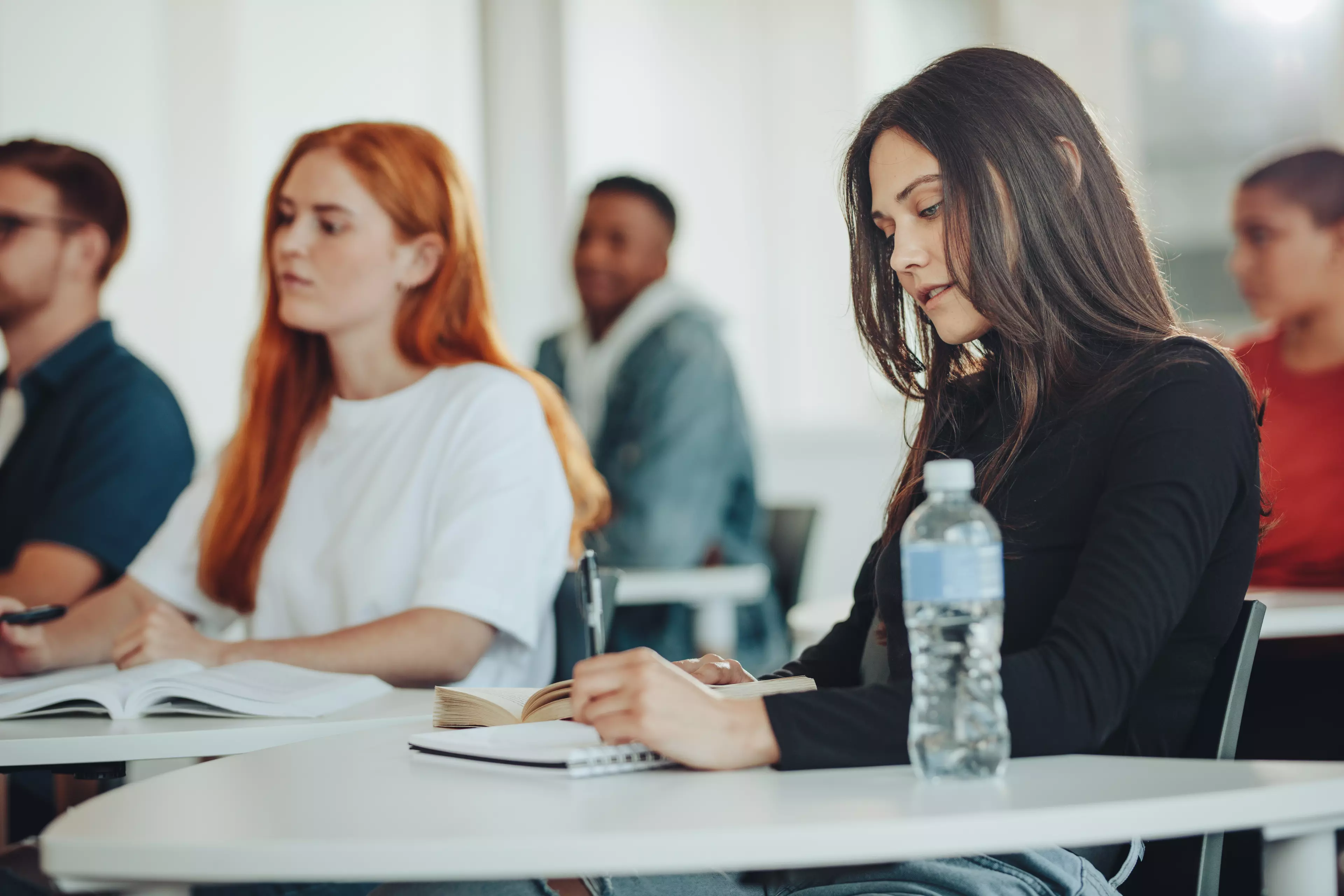  Young adult learners behind desks in the classroom, taking notes.