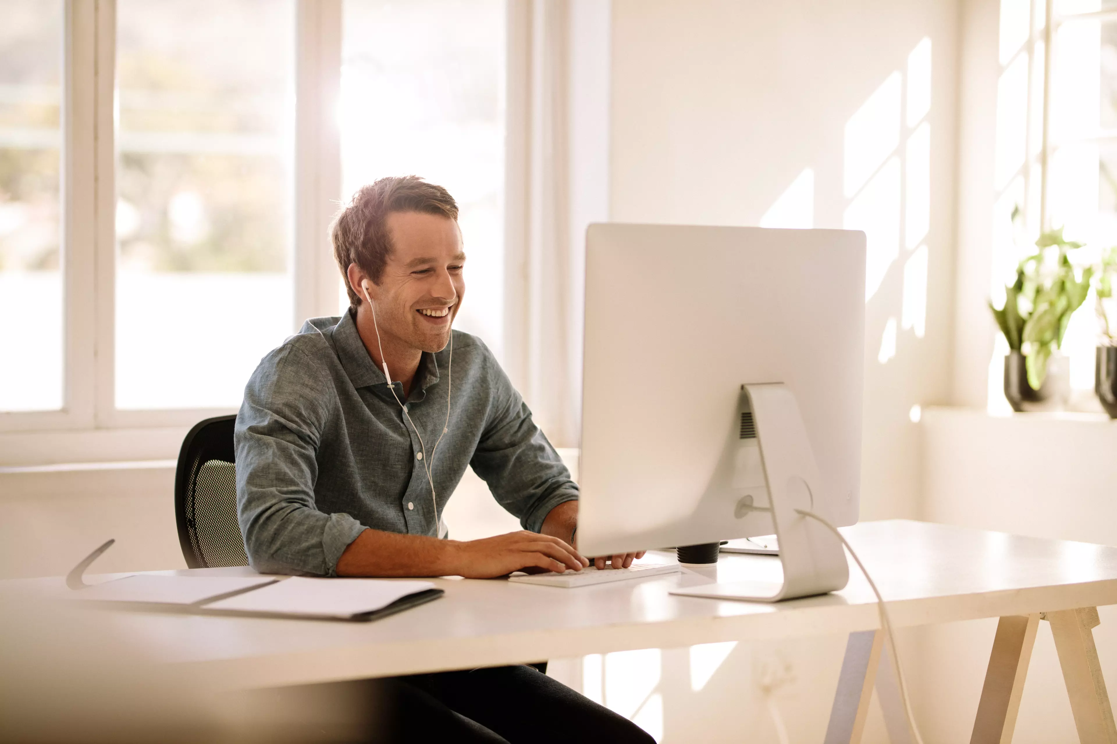 Smiling young man sitting behind a desk with talking over computer video messenger.